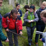 students gathered around a professor looking at soil in the forest