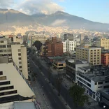view of an empty road going through Quito from on top of a tall building with the city and mountains in the distance