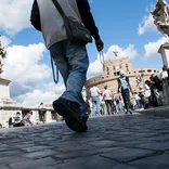 close up of a street vendor's feet as he walks down a cobblestone path towards the Colosseum
