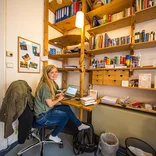 student sitting behind a wooden desk with bookshelves filled with German books on the wall in front of her
