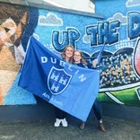 two student standing in front of a mural holding a large Dublin flag