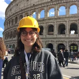 student wearing a yellow hard hat, standing in front of the Colosseum