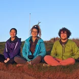 three students sitting on a grassy hill at sunset in Ireland