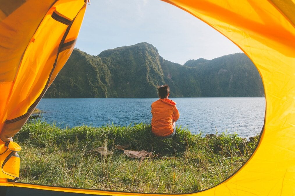 Person sitting outside of tent looking at water and hills