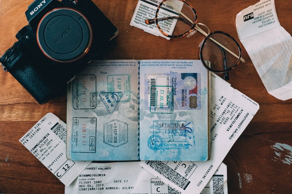 Photo by ConvertKit on Unsplash An open passport sits on a table next to a pair of glasses and a camera.