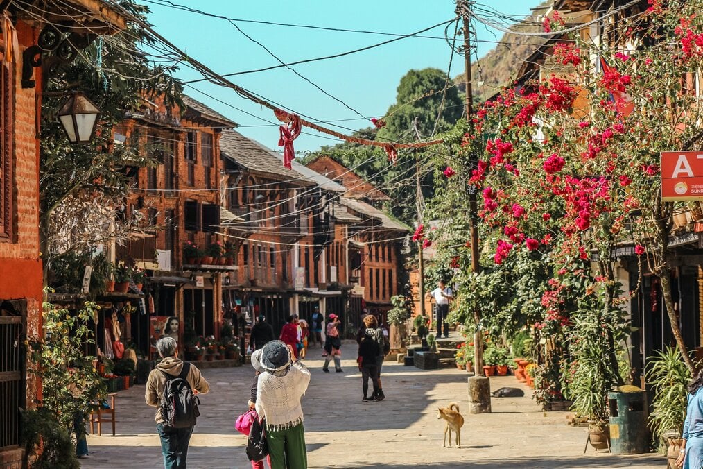 Photo by Samrat Khadka on Unsplash People walk down a street lined with vegetation and buildings in Bandipur, Nepal.
