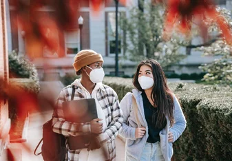 Two students walking through campus wearing masks