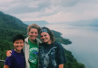 Three volunteers smiling in front of a hill and body of water