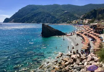An elevated view of an Italian beach surrounded by aqua blue water and mountains in the backdrop